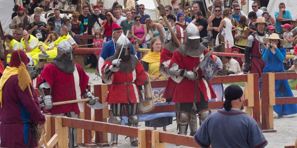 Cavalieri in armatura si sfidano in un evento medievale, con spettatori in abiti storici tutt’intorno.